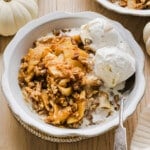 Apple pumpkin crisp with vanilla ice cream in a white bowl.
