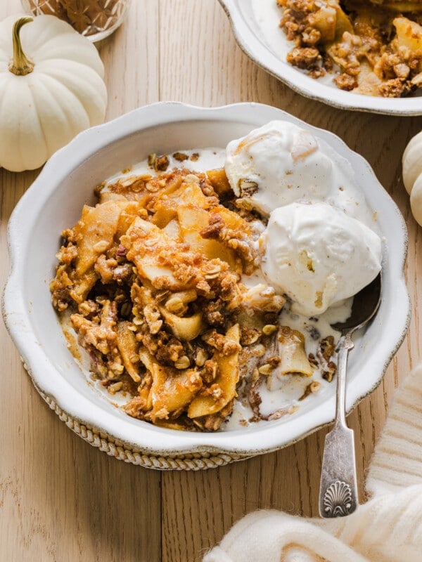 Apple pumpkin crisp with vanilla ice cream in a white bowl.