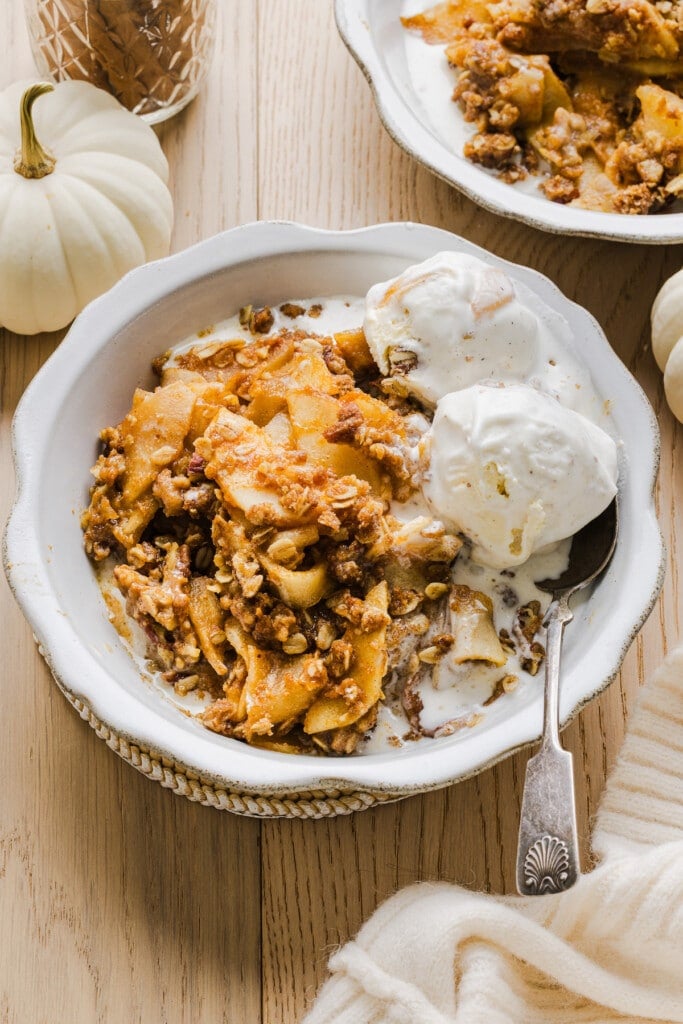 Apple pumpkin crisp with vanilla ice cream in a white bowl.