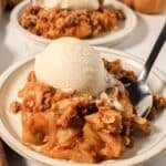 Two plates of pumpkin apple crisp topped with vanilla ice cream.