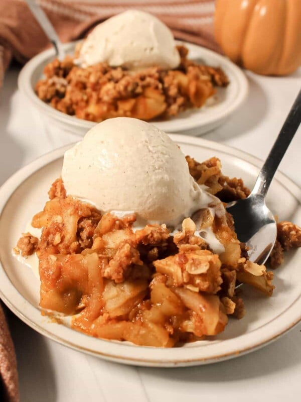 Two plates of pumpkin apple crisp topped with vanilla ice cream.