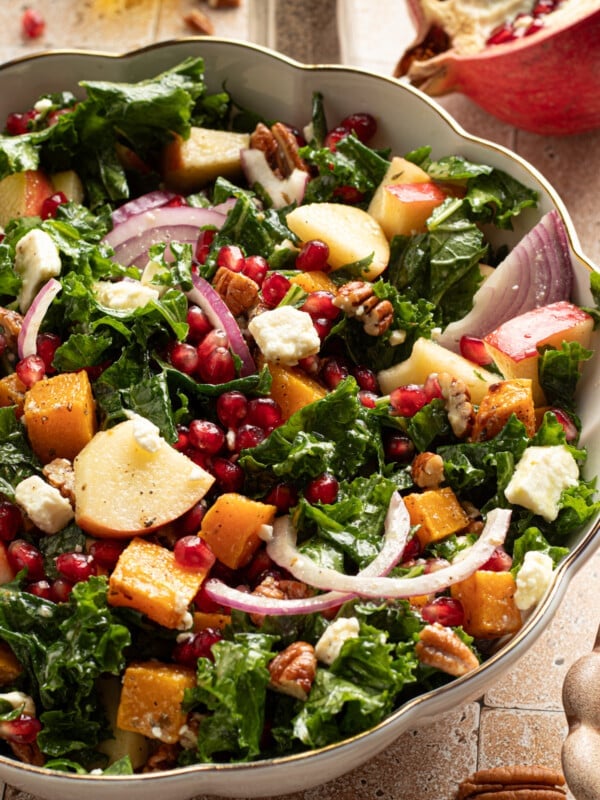 Kale and butternut squash salad with apple and pomegranate seeds in a large bowl.