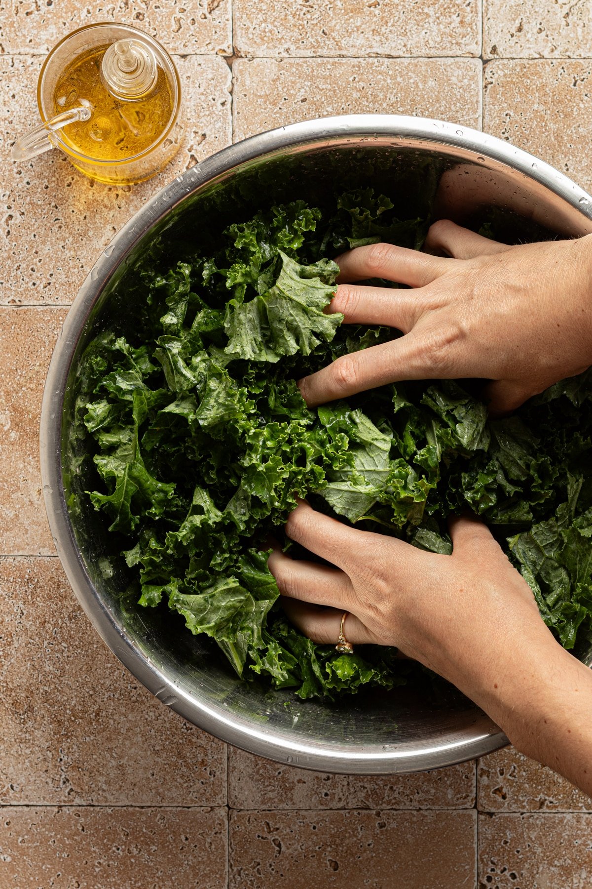 A bowl of kale being massaged with olive oil.