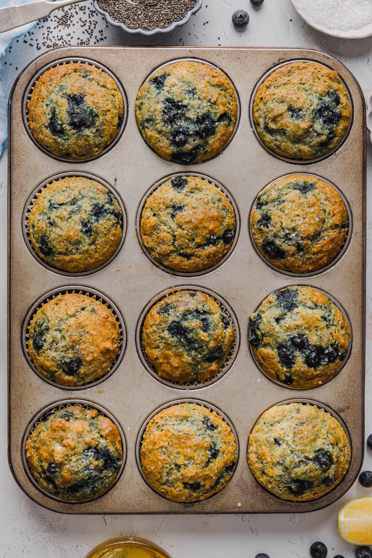 Blueberry chia muffins in a muffin tin on a white countertop after baking.