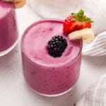 A blackberry smoothie garnished with blackberry strawberry and banana in a glass.