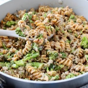 Ground turkey alfredo pasta with broccoli in a pan, with a large serving spoon scooping out a spoonful.