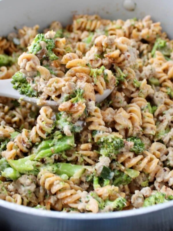 Ground turkey alfredo pasta with broccoli in a pan, with a large serving spoon scooping out a spoonful.