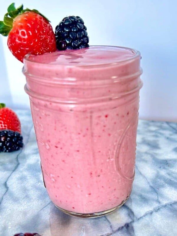 Blackberry strawberry banana smoothie in a glass jar topped with a fresh strawberry and a fresh blackberry.