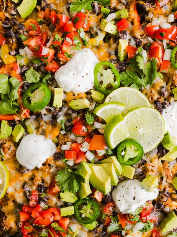 A close up shot of bell pepper nachos on a sheet pan with nacho toppings and sour cream.