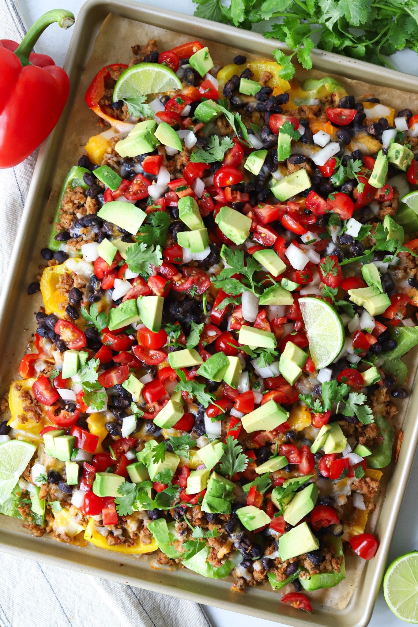 Bell pepper nachos made with nutritious ingredients like bell peppers, lean meat and beans and topped with your favorite nacho toppings. Bell pepper nachos on a sheet pan topped with pico de gallo, avocado and cilantro.