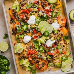 Bell pepper nachos on a sheet pan with nacho toppings and sour cream.