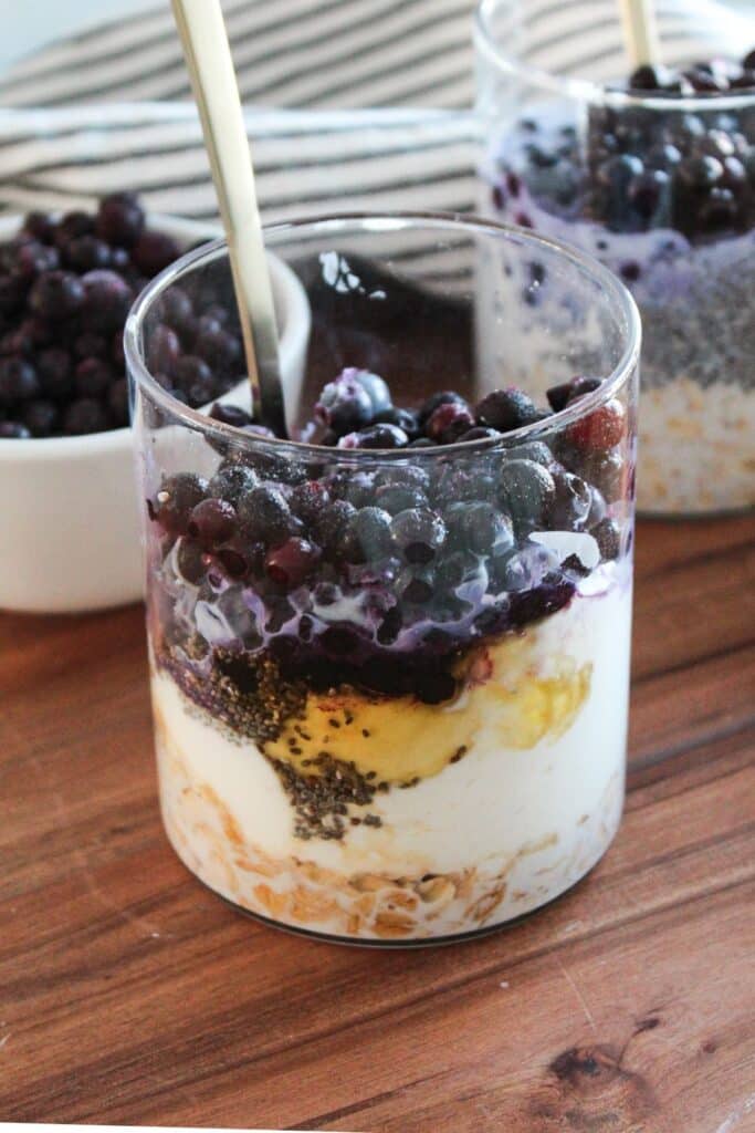 A jar with the ingredients for blueberry cheesecake overnight oats layered but not yet mixed.