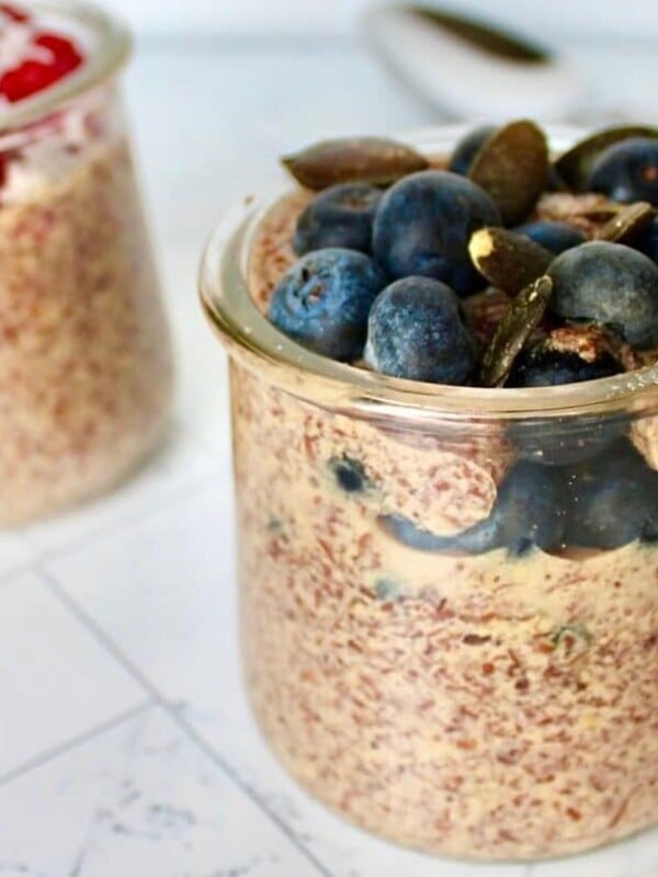 Two jars of flaxseed pudding, one with raspberries and coconut, one with blueberries and pumpkin seeds.