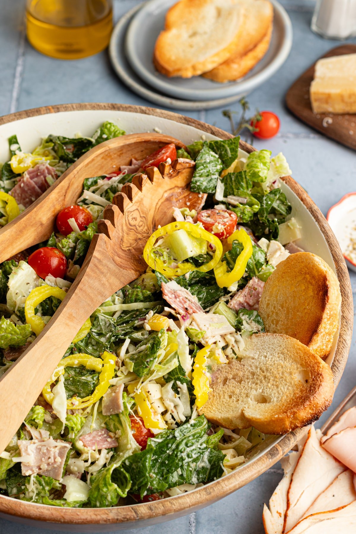 Italian grinder salad in a bowl with crostini and tongs.