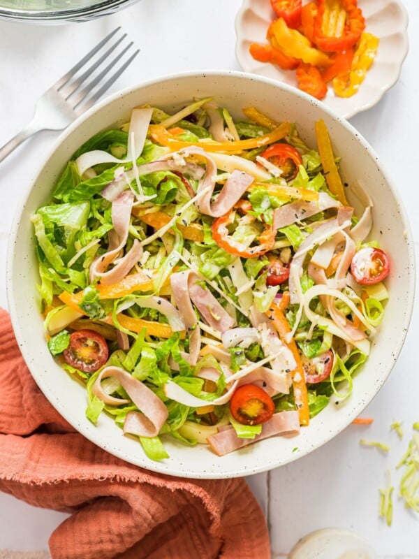 A birds eye shot of a grinder salad in a white bowl dressed with dressing on a white countertop.