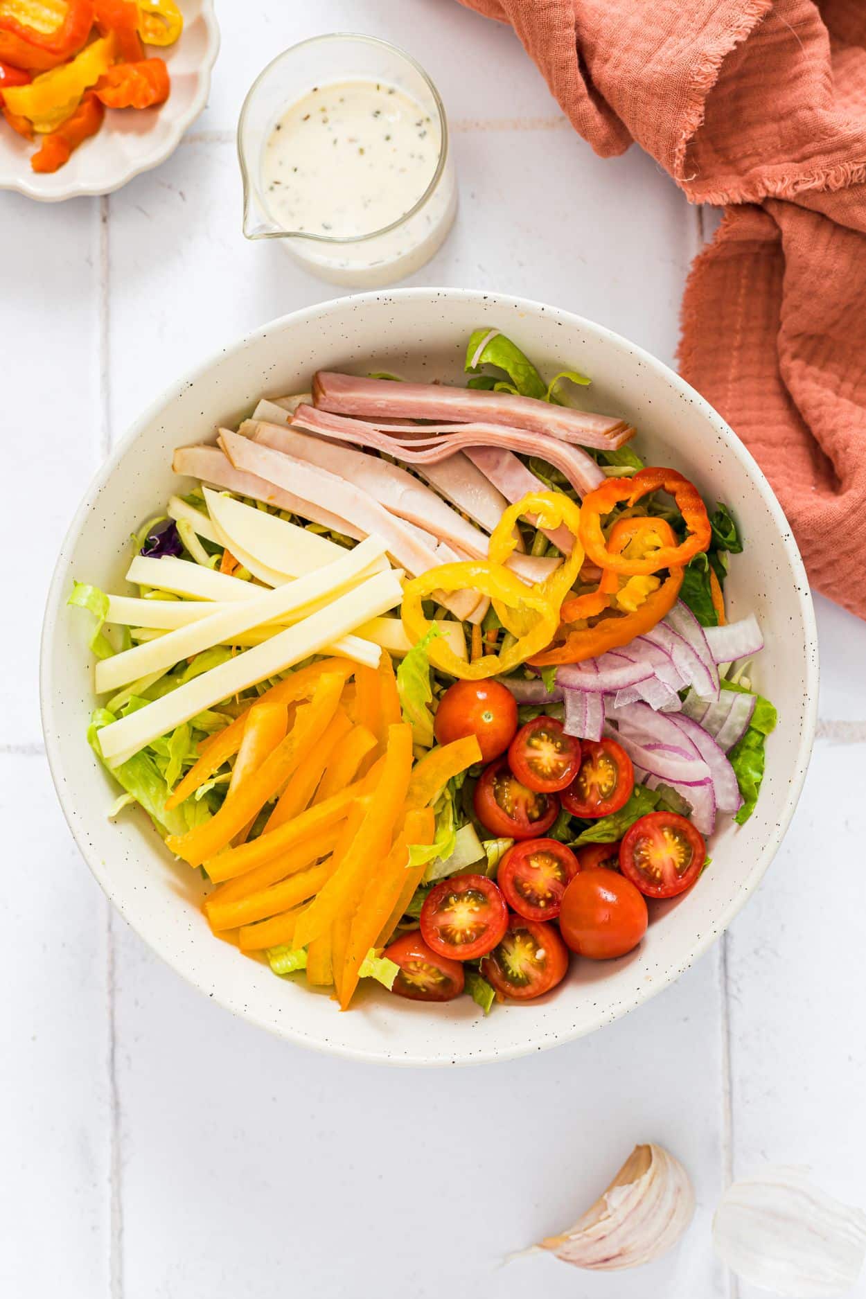 A white bowl with lettuce, tomatoes, bell pepper, provolone cheese, deli meats and banana peppers unmixed.