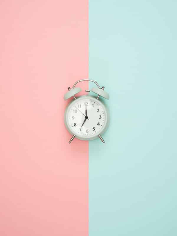 An old-fashioned alarm clock in front of a two-tone pink and blue background.