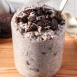 A clear glass jar of overnight oats with crumbled oreo cookies on top.