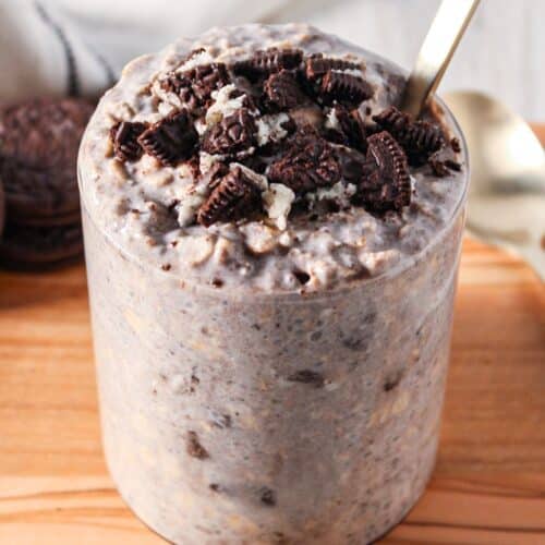 A clear glass jar of overnight oats with crumbled oreo cookies on top.