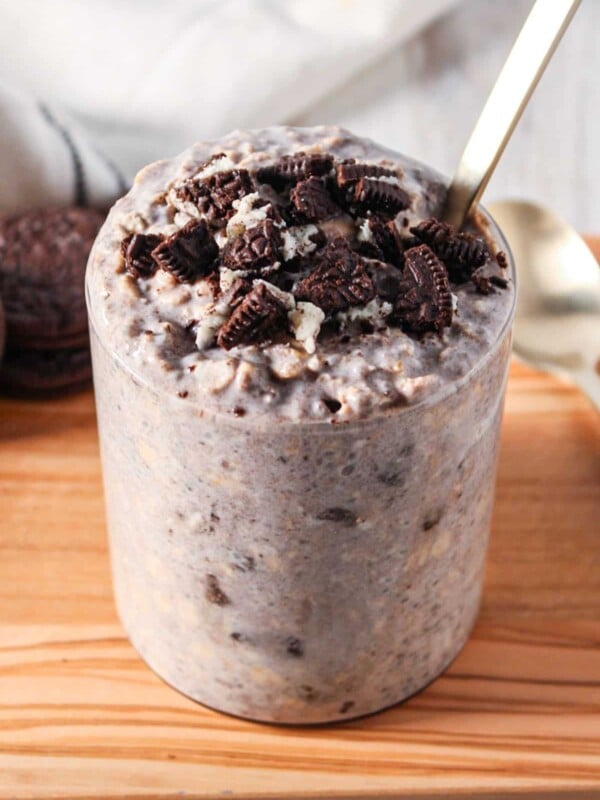 A clear glass jar of overnight oats with crumbled oreo cookies on top.