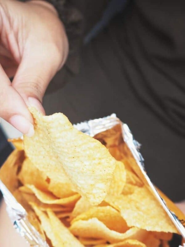 A hand grabbing some chips out of a chip bag.