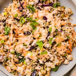 Inside out egg roll bowl in a plate with sriracha mayo on top.