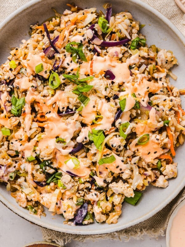 Inside out egg roll bowl in a plate with sriracha mayo on top.