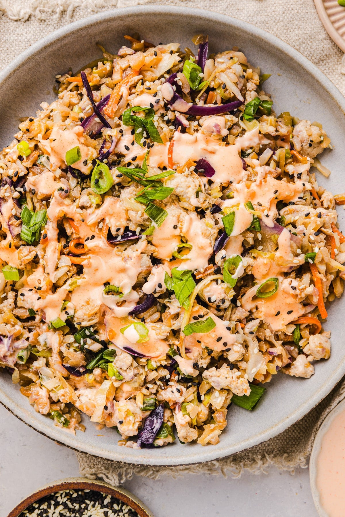 This is the BEST egg roll in a bowl recipe! It takes less than 20 min and uses one pan. An easy, satisfying dinner idea everyone loves. Inside out egg roll bowl in a plate with sriracha mayo on top.