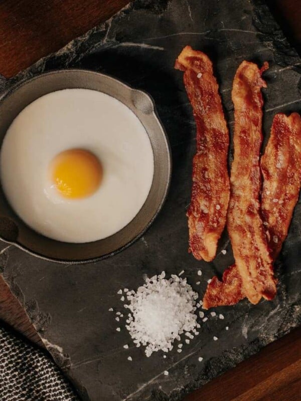 a 30 day keto challenge breakfast of bacon and an egg on a black countertop.