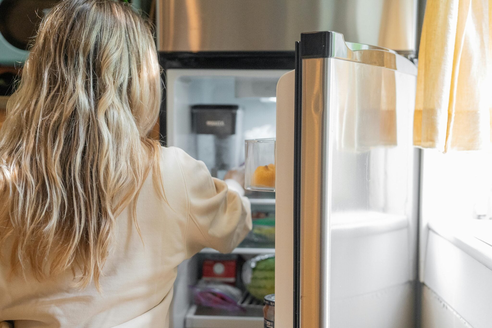 A woman looking into a fridge full of food, deciding what to eat.