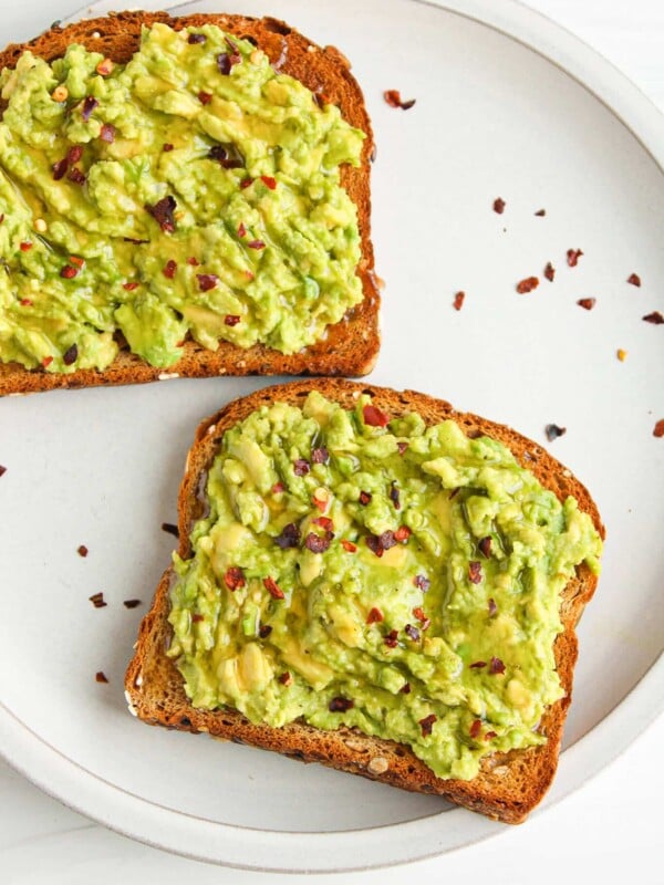 Two slices of avocado toast with honey on a plate sprinkled with red pepper flakes.