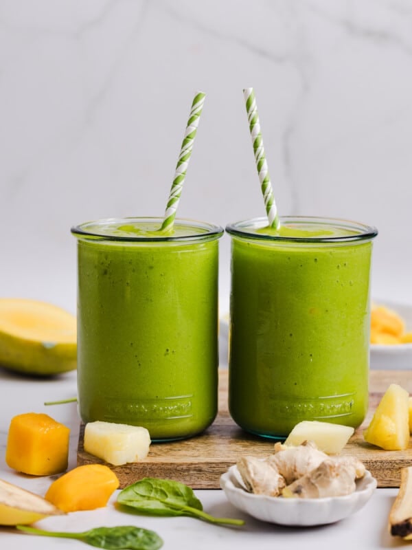 A green smoothie poured into two glasses with straws.