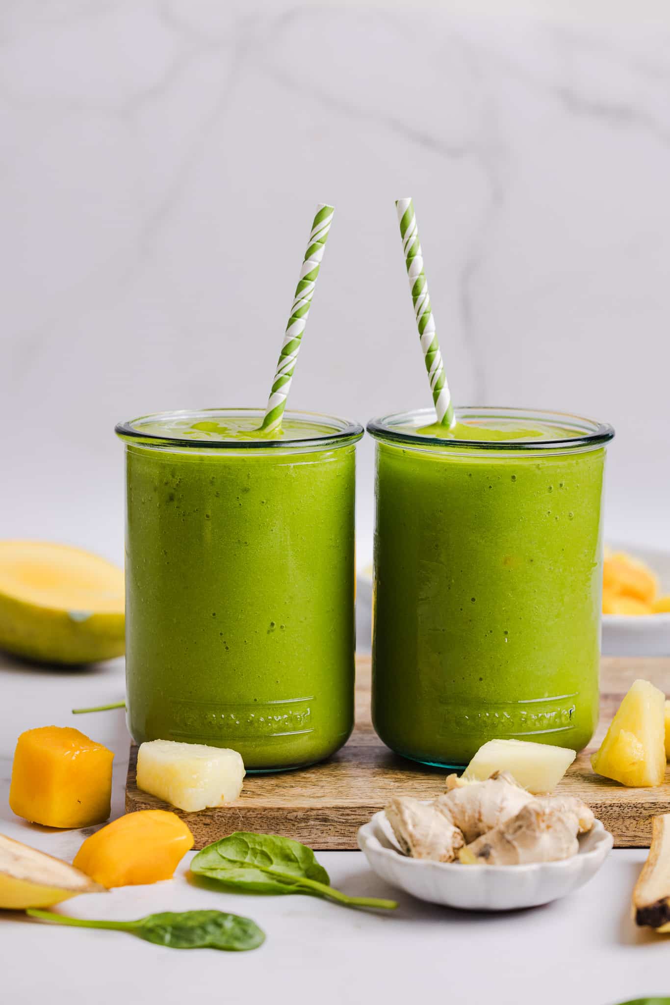 A green smoothie poured into two glasses with straws.