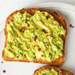 One slice of avocado toast with honey on a plate.