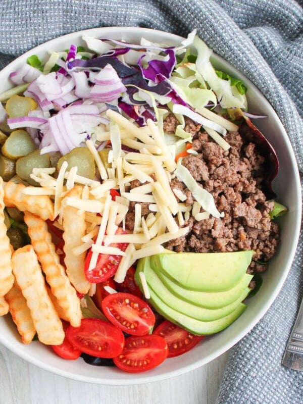 A deconstructed burger salad bowl on a countertop with a napkin and fork.