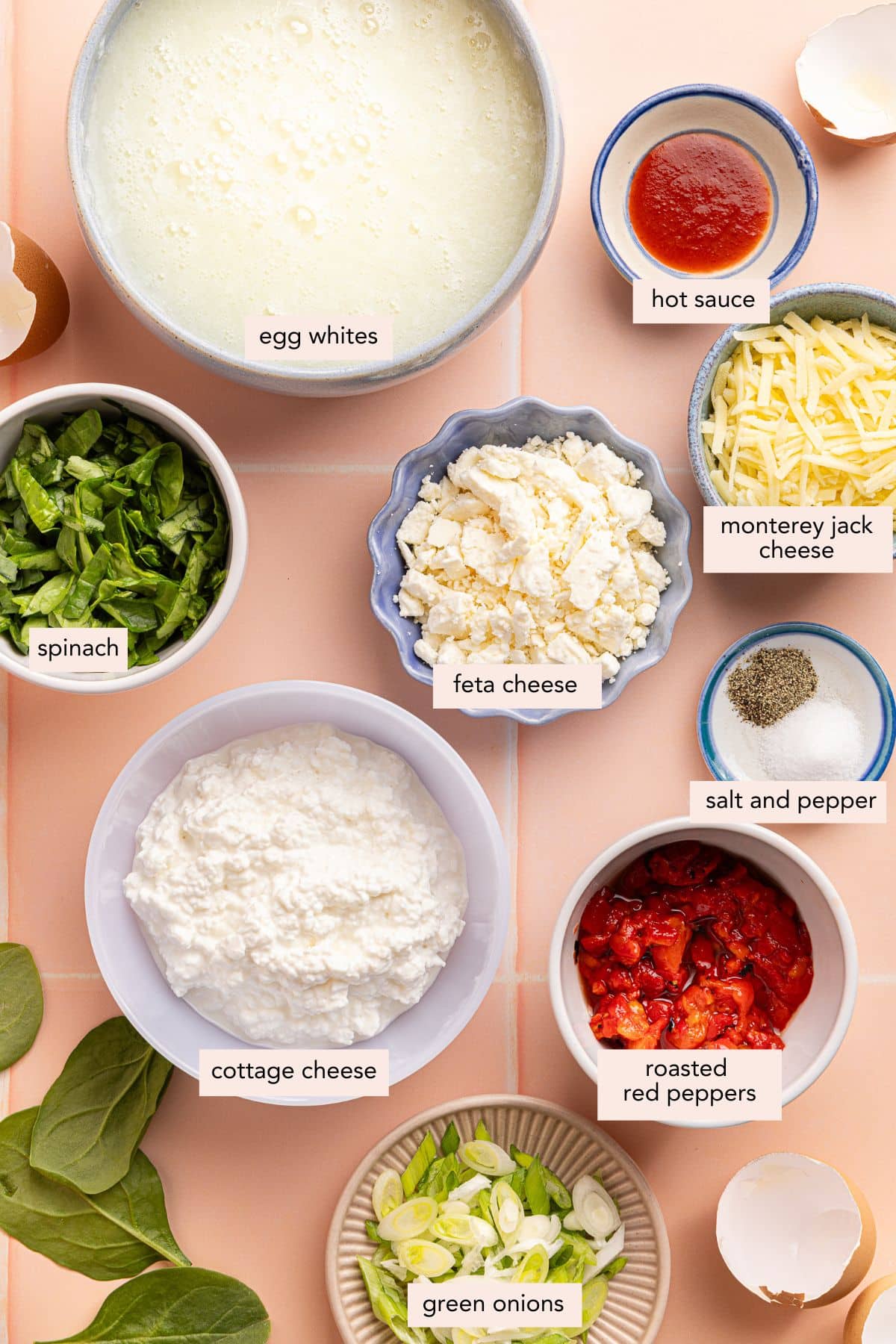 All of the ingredients for roasted red pepper egg white bites in bowls on a a countertop.