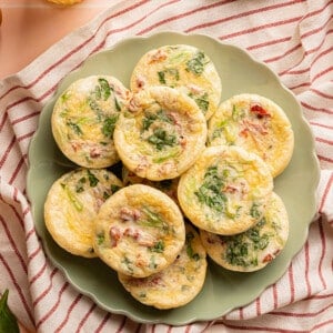 10 roasted red pepper egg white bites sitting on a green plate on top of a red stripped towel on a countertop.
