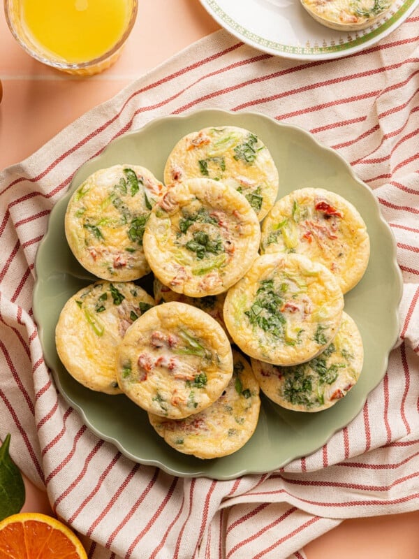 10 roasted red pepper egg white bites sitting on a green plate on top of a red stripped towel on a countertop.