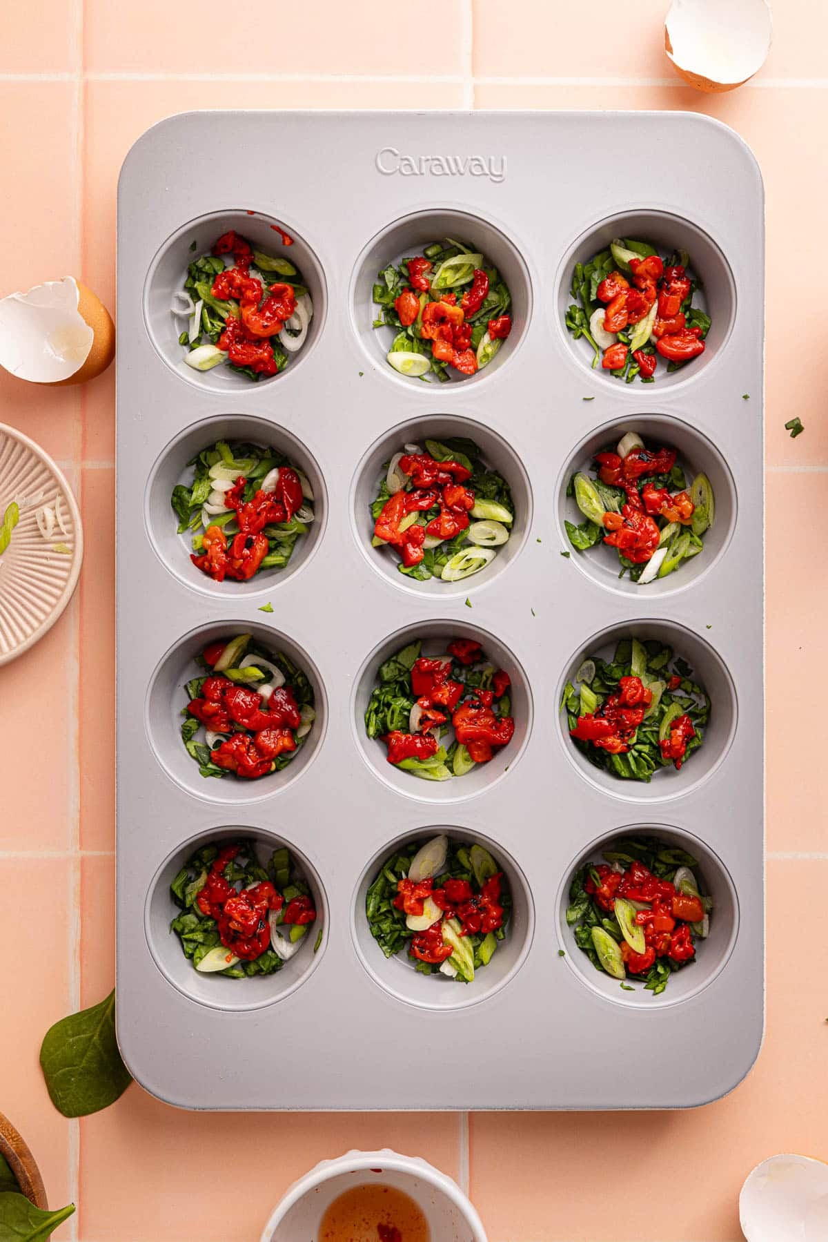 The spinach, green onions, and roasted red peppers layers in each cup of the prepared muffin tin.