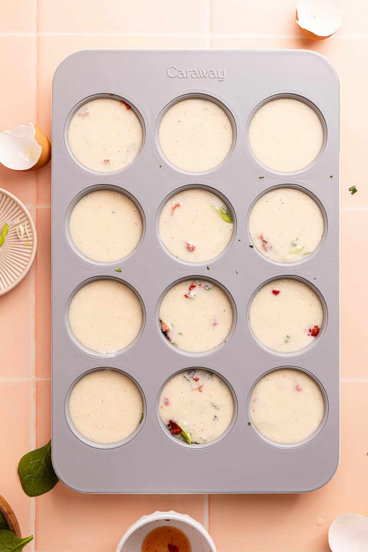 The egg mixture in the muffin tin over the veggie ingredients before baking in the oven.