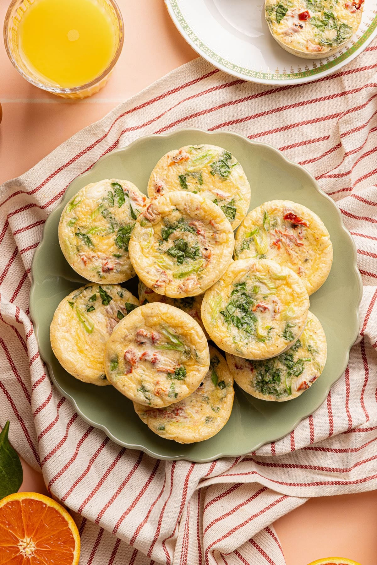 10 roasted red pepper egg white bites sitting on a green plate on top of a red stripped towel on a countertop.