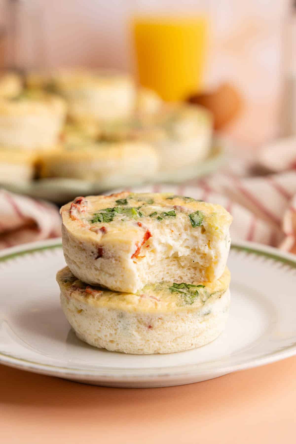 Two red pepper egg bites stacked on a plate. The top one has a bite taken out of it.