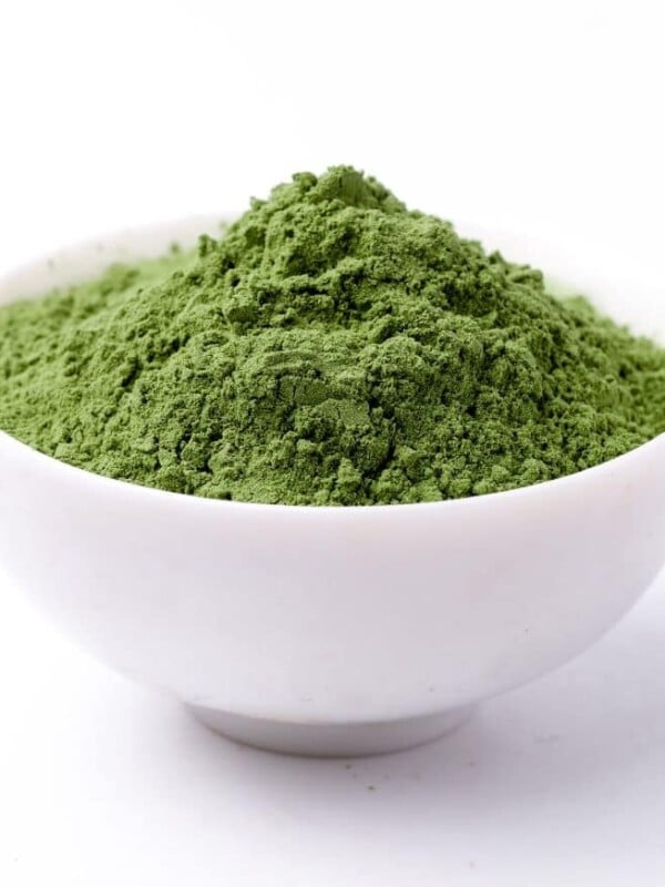 A ceramic white dish full of athletic greens powder on a white background.
