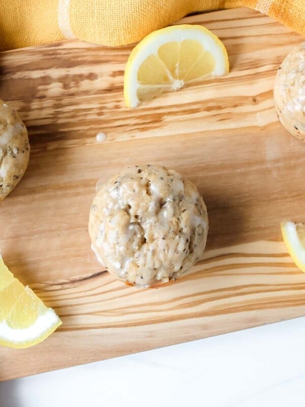 Lemon chia seed muffins on a wooden serving board, presented with sliced lemons and a yellow kitchen towel.