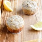 A close up shot of lemon seed muffins arranged on a wooden serving board with sliced lemons.