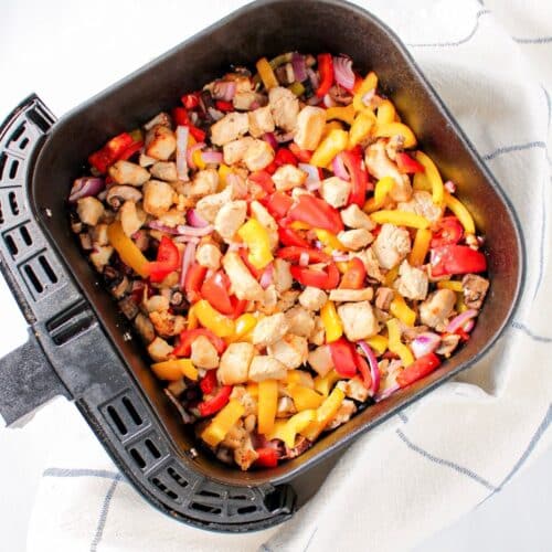 Air fryer stir fry chicken and vegetables in an air fryer basket.