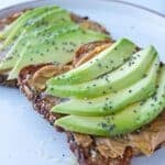 Peanut butter and avocado toast on a white plate sprinkled with chia seeds.
