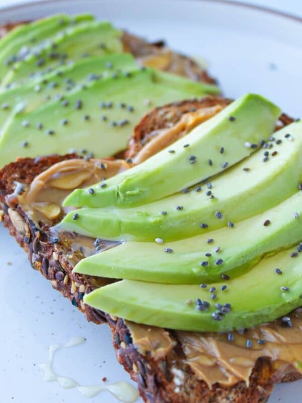 Peanut butter and avocado toast on a white plate sprinkled with chia seeds.