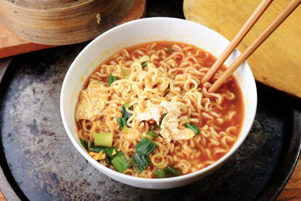 A bowl of ramen with green onions and chopsticks in a white bowl.