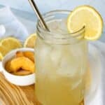 A large mason jar full of iced peach green tea lemonade, garnished with lemon.